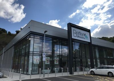 Exterior view of a modern bathroom store with large glass windows under a blue sky with clouds.