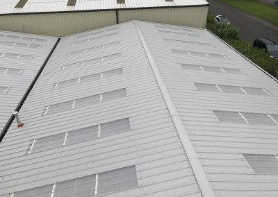 Aerial view of large industrial metal roofs, featuring multiple rows of white panels with skylights.