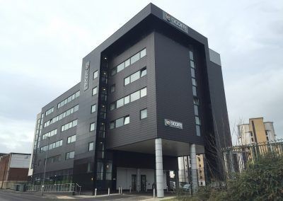 Modern multi-story office building with black exterior and numerous windows, located on an urban street.