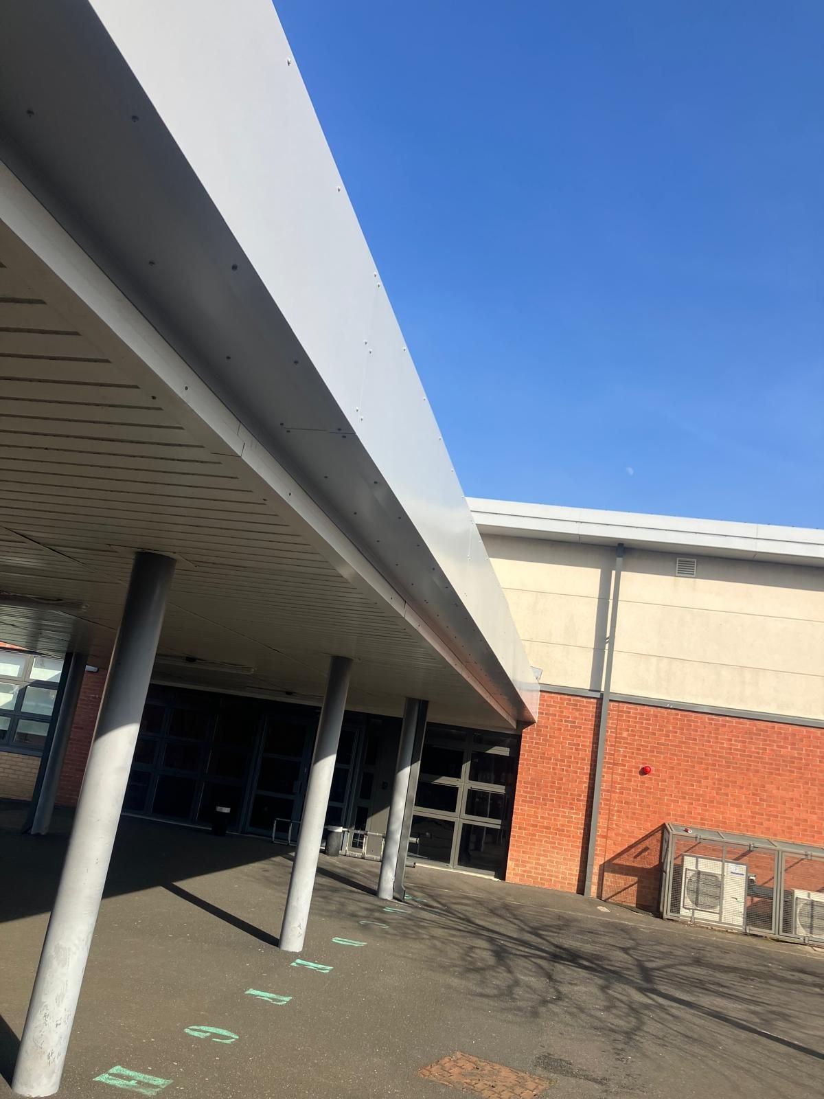 Exterior view of a modern building with metal supports and brick walls under a clear blue sky.